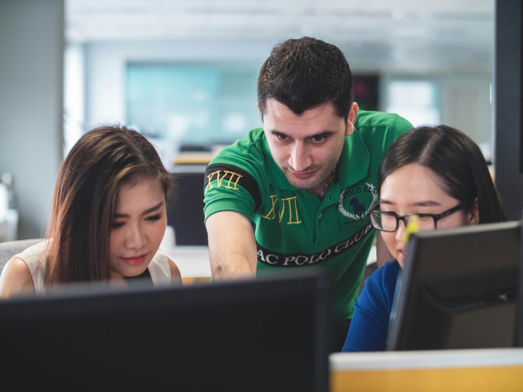 Faculty member points at computer screen while talking to two students.